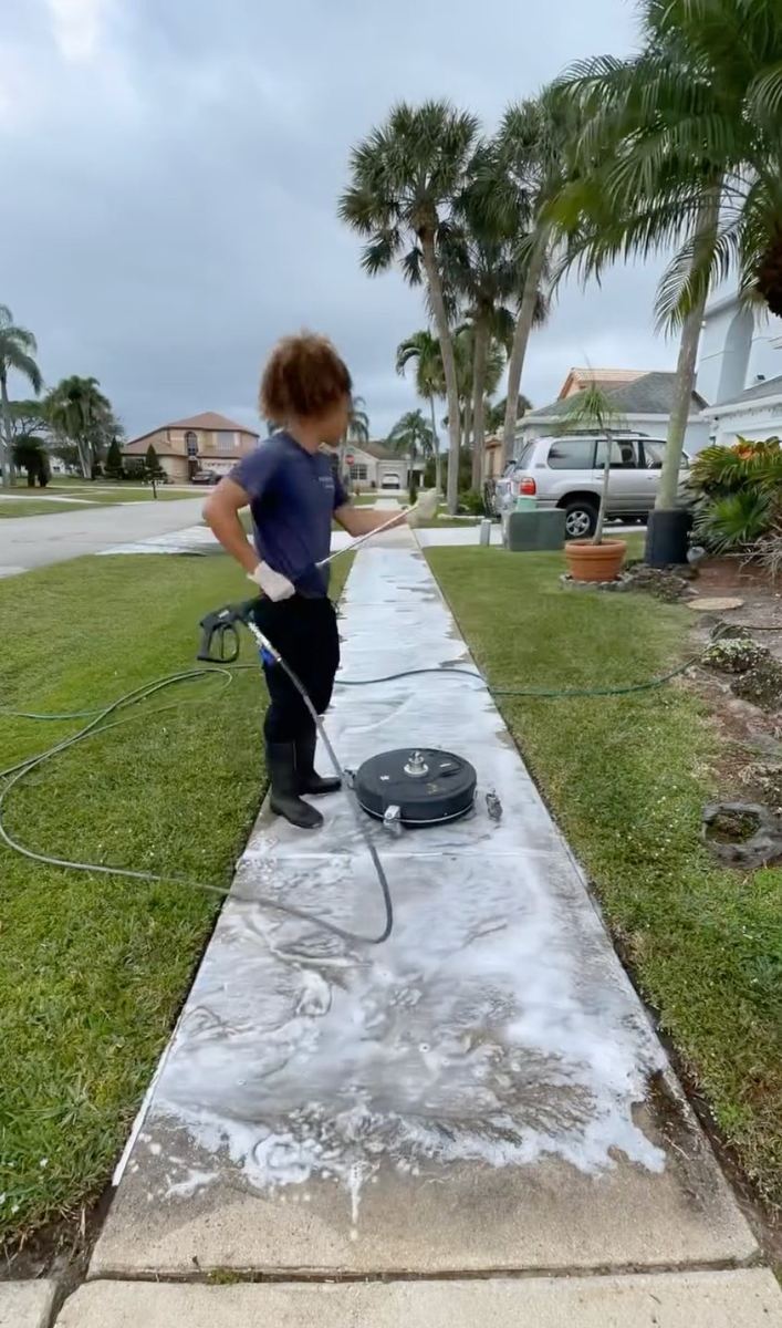 Soft-washing a concrete sidewalk with cleaning chemical in a South Florida neighborhood