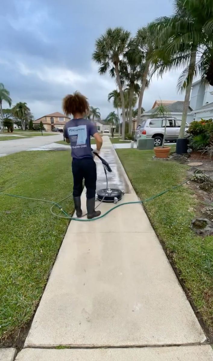 Pressure washing technician using a surface cleaner on a residential sidewalk in Boca Raton
